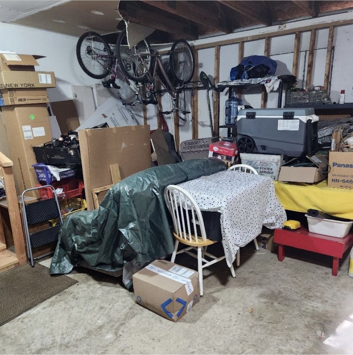 Packed garage with a tarp-covered sofa, bikes, boxes, and clutter before cleanout — Chantilly, VA